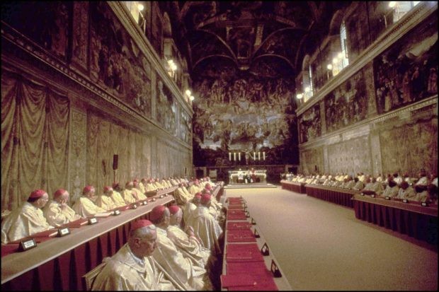 Cardinals dressed in white sit in rows in the Sistine Chapel