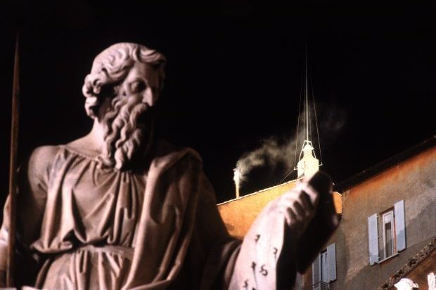 A statue in the foreground, a chimney emitting white smoke in the background